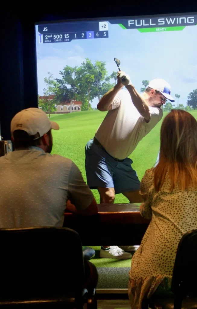 golfer using indoor golf simulator while friends watch